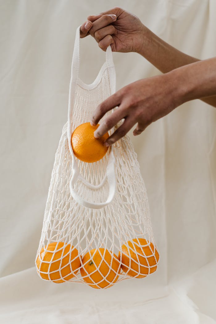 our-services-1 Hand holding a reusable mesh bag filled with fresh oranges, promoting sustainability and zero waste shopping.