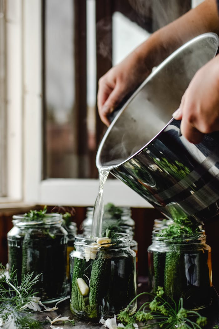 why-choose-us Fresh cucumbers being pickled in glass jars with herbs for homemade preservation.